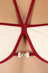 Top de bikini bandeau blanco marfil con ribete rojo oscuro. Tiene tiras que se anudan al cuello para un amarre halter, adornadas con delicados detalles de cuentas doradas.
