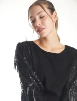 Buzo de tejido negro con mangas largas de microtul transparente, decoradas con bordados de lentejuelas y flecos brillantes. Presenta un diseño elegante con cuello redondo.