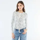 Camiseta de manga larga confeccionada en tejido de punto calado, con estampado de pequeñas flores azules sobre fondo blanco. Presenta un diseño ajustado al cuerpo, cuello redondo y una pequeña abertura frontal con botones.