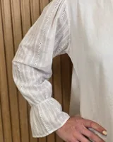 Blusa blanca de algodón con escote en V y cuello mao. Presenta mangas largas abullonadas con puños acampanados y fruncidos.