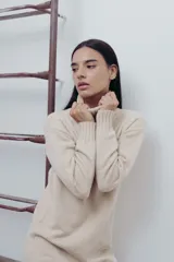 Vestido corto de tejido de punto en color beige, con cuello alto y mangas largas. Presenta puños y ruedo acanalados, con un diseño de calce relajado.