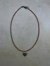 Collar de tres niveles compuesto por cuentas pequeñas de piedra natural y metal, con tres dijes en forma de corazón de piedra natural facetada en tonos rosado, negro y gris, enmarcados en metal dorado.