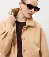 Campera de gamuza sintética color tostado con botones dorados grabados, cuello camisero, bolsillos frontales aplicados y mangas largas con puños abotonados.