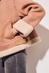 Campera gamulan color rosa con interior de piel sintética color crema, cierre frontal con cremallera y hebillas en el cuello. Corte oversize.