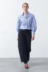 Camisa a rayas azules y blancas de manga larga, con cuello clásico y puños abotonados. Presenta un diseño entallado en la cintura.