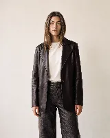 Blazer sastre confeccionado en 100% cuero bovino, de color marrón oscuro, con solapas clásicas, cierre frontal de un botón y bolsillos con solapa en los laterales.