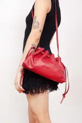 Bolso tipo sobre de cuero color rojo, con frunce superior y cierre con cordones. Tiene correa larga desmontable y bolsillo interno con cierre.