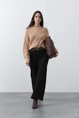 Polera tejida de color beige con cuello alto, mangas largas con puños ajustados y silueta relajada.