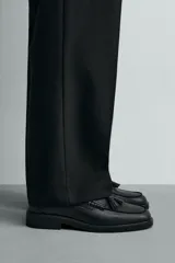 Mocasín de vestir color marrón oscuro, confeccionado en cuero, con detalle de antifaz y borlas en el empeine, horma redonda y suela plana a tono.