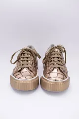 Zapatillas bajas color dorado con diseño trenzado, cordones y suela de goma.