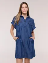Vestido camisero corto de jean color azul, con cuello camisero, escote en V y botones frontales parciales. Tiene mangas cortas con dobladillo y bolsillos con solapa en el pecho.