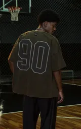 Remera de manga corta y cuello redondo, calce oversize, color marrón oscuro con efecto batik artesanal. Presenta un estampado frontal con la palabra "RAVERS" en tipografía universitaria con borde blanco.