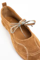 Chatita de gamuza color camel con costuras decorativas en hilo blanco y cordones ajustables en la parte superior. Presenta suela de goma dentada y tirador en el talón.