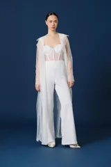 Mono largo color blanco de la marca Natalia Antolín, con diseño strapless con tirantes, cuerpo estilo corset de encaje semitransparente con ballenas visibles y parte inferior de pantalón recto de vestir.