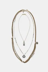 Pack de tres collares superpuestos de metal en tonos dorado y plateado. El collar más corto tiene un dije colgante en forma de reloj ovalado con piedras de colores. El collar intermedio tiene un dije colgante en forma de reloj redondo con marco floral. El collar más largo consiste en múltiples cadenas finas, algunas con cuentas, y un dije colgante en forma de estrella de múltiples puntas.