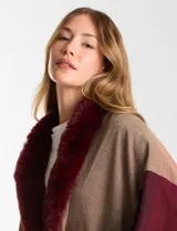 Ruana tejida con diseño de bloques de color en tonos tierra y bordó, con cuello de piel sintética en color bordó y terminación de ruedo con flecos.