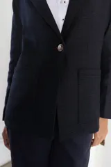 Blazer femenino forrado de corte tradicional, levemente entallado en la cintura, con mini hombreras. Presenta un botón metálico decorativo con escudo y costuras en tono contraste.
