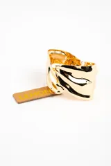 Brazalete rígido de metal dorado con diseño de superficie ondulada y brillante.