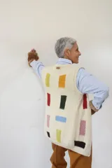 Chaleco tejido a mano en lana merino, con escote en V, cierre frontal de botones de madera y diseño con detalles geométricos de colores.