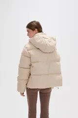 Campera puffer color beige con diseño capitoneado, capucha integrada y cierre frontal oculto. Presenta bolsillos laterales y un corte holgado.