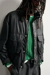Cazadora regular fit de Zara en colaboración con Aaron Levine, confeccionada en tejido de algodón con acabado efecto encerado en color negro. Presenta cuello subido, manga larga con puño ajustable, bolsillos frontales con solapa y cierre de cremallera oculto con solapa de botones a presión.