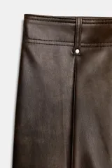 Pantalón de tiro alto color marrón oscuro con efecto piel, pierna ancha y costura marcada en el delantero. Incluye bolsillos de plastrón en la espalda y cierre frontal con cremallera, botón y gancho metálico.