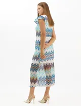 Vestido midi confeccionado en tejido de punto calado, con patrón geométrico en zigzag en tonos blanco, marrón, tostado y azul. Presenta escote a la base, mangas cortas con volados en los hombros, silueta recta y forro interior a tono. Incluye un cinturón fino con hebilla metálica.