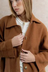 Chaqueta corta tipo blazer color marrón, confeccionada en tela de lana afieltrada. Tiene cuello camisero, silueta cuadrada, cierre frontal con botones y bolsillos delanteros.