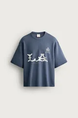 Camiseta azul de corte relaxed fit, con cuello redondo, mangas cortas y estampado frontal con la inscripción "L.A. California" y detalles gráficos.