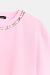 Remera de algodón color rosado, con cuello redondo decorado con una aplicación de joyas y pedrería, manga corta y corte regular.