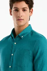 Camisa de lino de manga larga color verde turquesa, con cuello camisero, cierre frontal de botones y un bolsillo ojal en el pecho.
