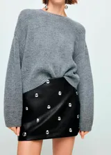 Minifalda de efecto piel en color negro, con corte recto y diseño adornado con tachuelas metálicas circulares distribuidas por toda la prenda. Cuenta con cierre de cremallera lateral y forro interior.