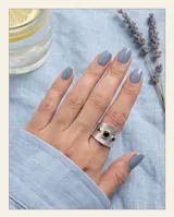Anillo ancho de plata 925 con textura martillada y detalles en oro de 18k, incrustado con tres circonias azules.