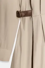 Vestido camisero corto color beige claro, con cuello solapa, manga larga y bajo tipo globo. Presenta detalles de cintas marrones con hebillas a la altura de la cintura.