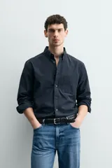 Camisa de corte regular fit confeccionada en tejido de algodón. Presenta cuello con solapa abotonada, cierre frontal con botones, manga larga con puños abotonados y un bolsillo plastrón en el pecho.