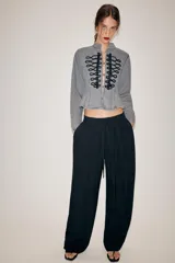Chaqueta de denim gris con cuello subido y manga larga. Presenta un diseño entallado con bajo en evasé y un llamativo bordado frontal de alamares en color negro. Cierre frontal con corchetes ocultos.