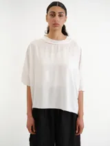 Remerón blanco de corte holgado, mangas cortas amplias y cuello bote con jareta.