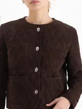 Chaqueta de cuero gamuzado color marrón con diseño matelaseado en toda la prenda. Presenta cuello redondo, cierre frontal con botones metálicos y cuatro bolsillos delanteros.