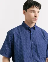 Camisa de manga corta azul con estampado de lunares blancos, cuello abotonado y bolsillo en el pecho.
