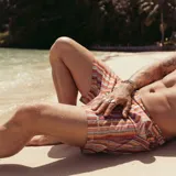 Short de baño con estampado geométrico en tonos tierra, naranja y violeta. Cuenta con pretina fija, hebillas metálicas laterales para ajuste, cierre frontal con botón a presión y tres bolsillos. Incluye interior con mesh hipoalergénico.