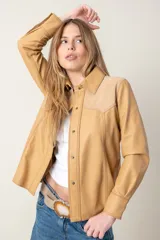 Camisa vaquera de cuero ovino italiano color camel, confeccionada a mano. Presenta canesú de gamuza en los hombros, broches metálicos frontales y en los puños, y bolsillos laterales.