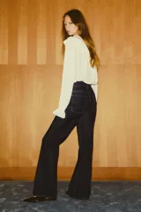 Jean de denim de algodón con leve stretch, color azul oscuro (índigo). Presenta un corte ajustado en la cintura y cadera, ensanchándose en un corte acampanado desde la rodilla hasta el bajo. Es de tiro alto con cierre y botones frontales, y cuenta con solapas decorativas en los bolsillos delanteros y bolsillos parche traseros.