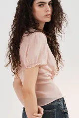 Top de georgette semitransparente color rosado, con cuello redondo, mangas cortas abullonadas y cierre frontal con botones. Presenta detalles de alforzas en la parte inferior.