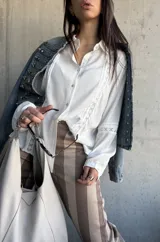 Camisa blanca de manga larga con detalles de encaje y calados verticales en el frente y las mangas.