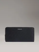 Billetera tipo organizador de Calvin Klein, confeccionada en piel sintética negra con estampado de monograma texturizado en toda la superficie. Cuenta con cierre perimetral de cremallera, múltiples ranuras para tarjetas, compartimentos para billetes y bolsillo interno para monedas. Incluye logo metálico de la marca en la parte frontal.