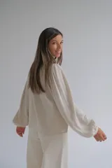 Blusa de color beige con cuello mao, cierre frontal con botones y mangas largas abullonadas. Presenta delicados bordados florales en la parte superior delantera.