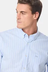 Camisa de corte clásico confeccionada en tela oxford de algodón, con diseño de rayas verticales finas en color celeste y blanco. Presenta cuello abotonado, cierre frontal con botones y bolsillo en el pecho.