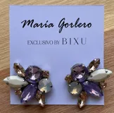 Par de caravanas con forma de flor, con cristales facetados en tonos lila, blanco y dorado.