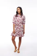 Vestido corto camisero blanco con estampado de motivos campestres en color bordó. Tiene cuello camisero, mangas 3/4, lazo en la cintura y volado en el ruedo.