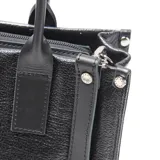 Cartera tipo tote de cuero negro con textura granulada, cuenta con doble asa de mano y correa larga ajustable y extraíble. Presenta el logo de la marca XL grabado en el frente.
